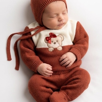 Bebê vestido com conjunto de malha cor ferrugem e branco, com desenho de urso, deitado sobre fundo branco.