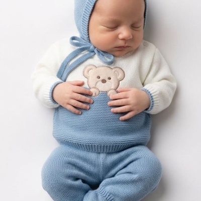 Bebé com roupa de malha azul claro e branca com ursinho bordado.