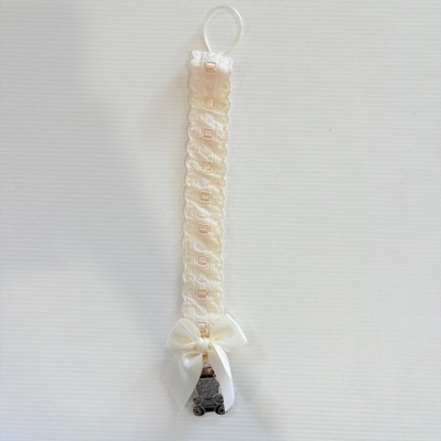 Fita decorativa bege com laço branco e pendente de ursinho metálico.