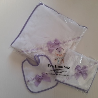 Conjunto de três peças para bebé com laços lilás e rendas, embaladas em plástico transparente.