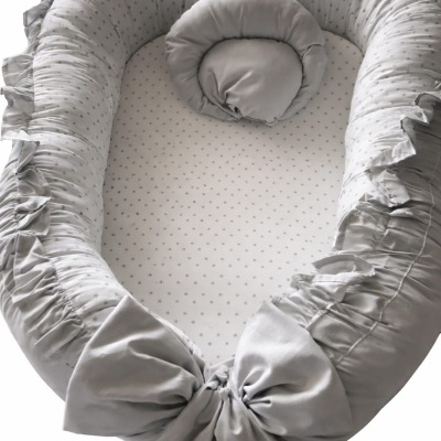 Cama de bebé cinzenta com almofada redonda e bordas almofadadas com rufos