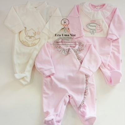 Três macacões de bebé em algodão rosa e branco com bordados e detalhes variados, mais um gorro rosa sobre fundo branco.