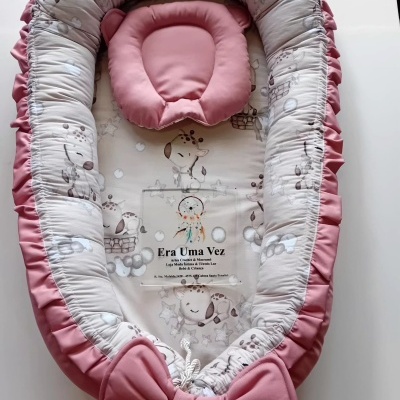 Ninho para bebé branco e rosa com padrões de girafas e almofada em forma de urso.