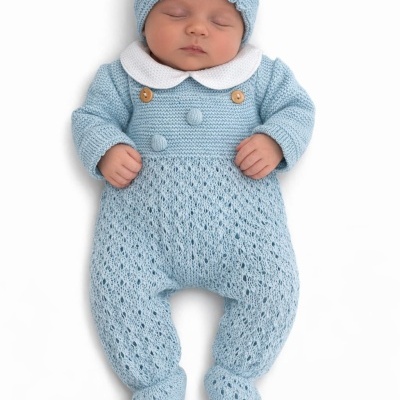 Bebé a dormir vestindo um macacão azul claro de malha com gola branca e touca azul da mesma malha.