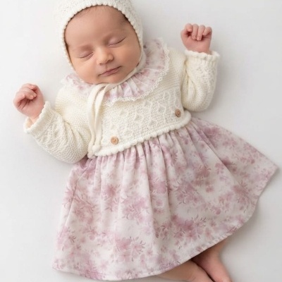 Bebé a dormir com conjunto de malha branca e vestido floral rosa
