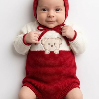 Bebé deitado com body vermelho e creme com ursinho bordado e gorro vermelho de malha