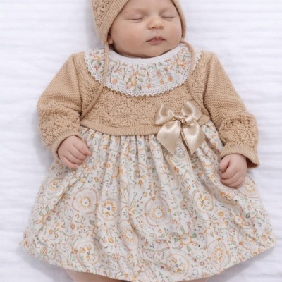 Bebé a dormir com vestido estampado e suéter de malha bege mais gorro da mesma cor