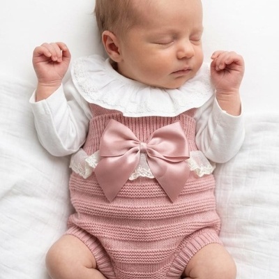 Bebé recém-nascido a dormir vestido com body branco e roupa de malha rosa com laço de cetim.