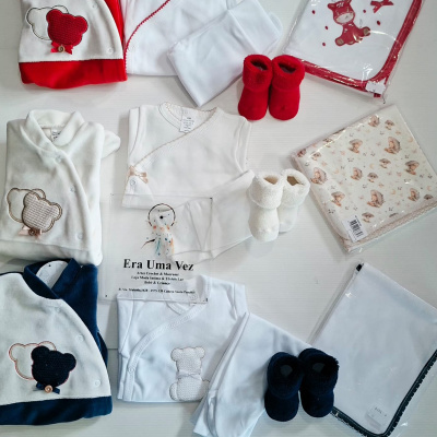 Conjunto de roupa de bebé com bordados de ursos em vermelho, branco, azul e bege com mantas embaladas e etiquetas visíveis.