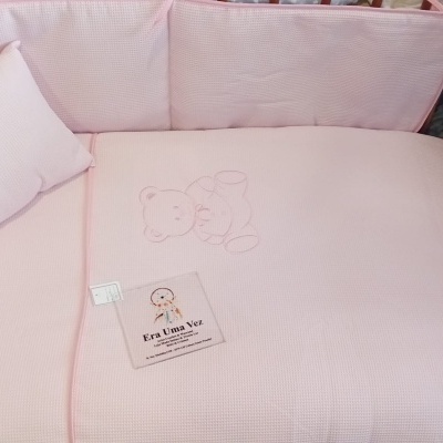 Berço de madeira com almofadas e colchão rosa claro e bordado de ursinho