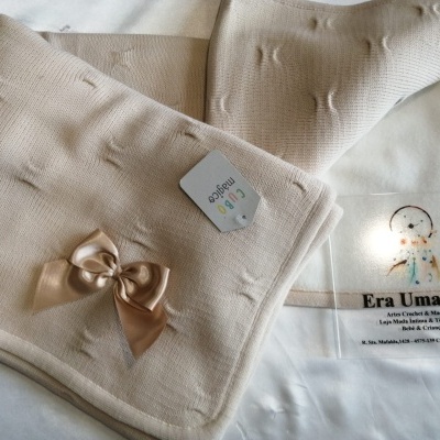 Roupas de bebé creme com laço e etiqueta Cubo magia sobre fundo branco com cartão da loja Era Uma Vez