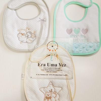 Três babygrows de tecido com padrões de pontos pequenos e bordados de ursos e corações sobre fundo branco