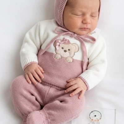Bebé com roupa de malha rosa e branca deitada ao lado de placa com texto informativo