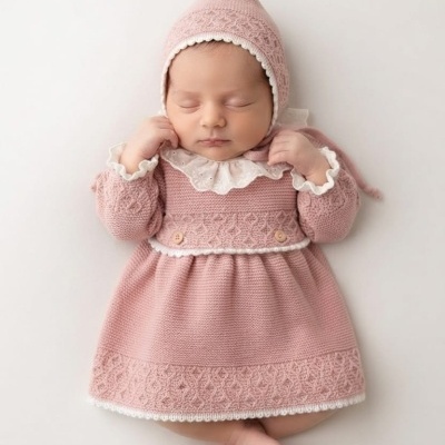 Bebé com vestido e chapéu de malha rosa adormecido em fundo branco