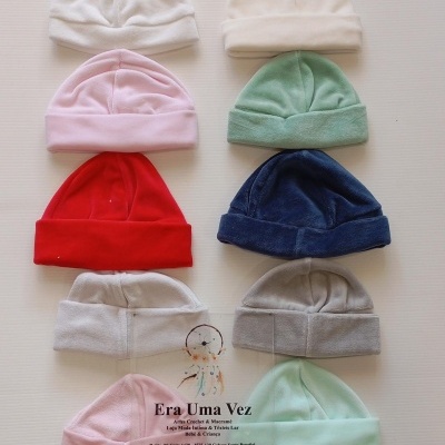 Gorros de bebé coloridos em tecido macio dispostos em fundo branco com etiqueta transparente