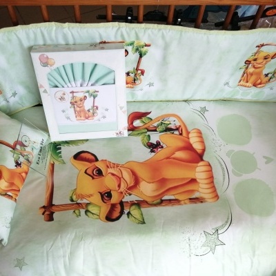 Roupa de berço verde clara com personagem Simba do Rei Leão em berço de madeira