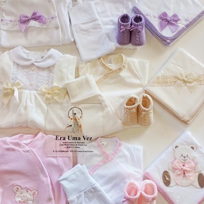Conjunto de roupa e acessórios para bebé em branco, rosa e bege com laços, rendas, sapatinhos de malha e mantas embaladas