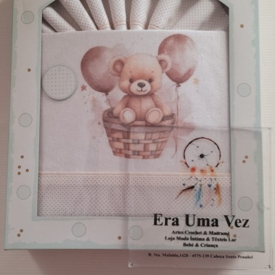 Conjunto de têxteis para bebé com desenho de ursinho num cesto com balões na embalagem.