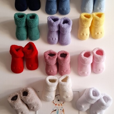 Dez pares de meias botins coloridas para bebé dispostos sobre uma superfície branca