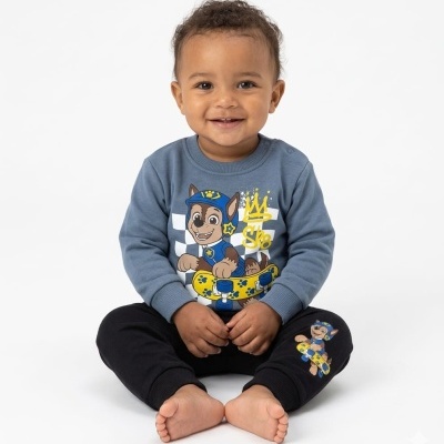 Bebé sentado com roupa azul e preta com estampa de cão e skate