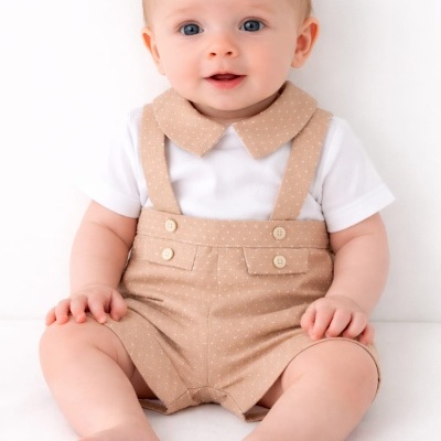 Bebé com body branco e calças bege com botões e alças sentado