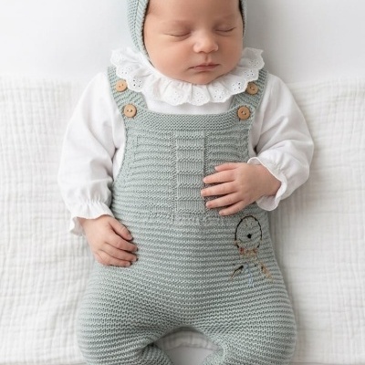 Bebé a dormir vestido com fato de malha verde claro, camisa branca com golinha bordada e gorro verde com pompom branco.