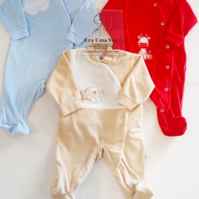 Três macacões de bebé em tecido macio, azul claro, vermelho e bege, com padrões de nuvem, vaca e urso.