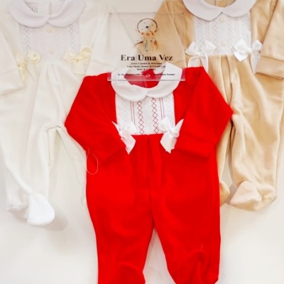 Três macacões de bebé de cores branca, vermelha e bege com golas brancas e laços decorativos