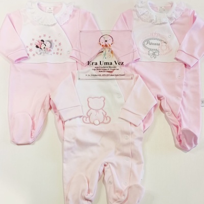 Três macacões de bebé cor-de-rosa e branco com estampados variados, colarinhos em renda, sobre fundo branco.