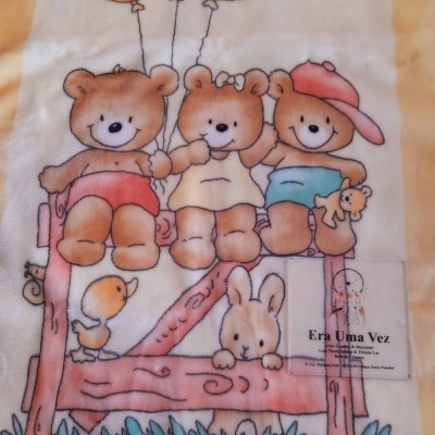Cobertor amarelo com desenho de três ursos a segurar balões sentados num banco com coelho e pato.