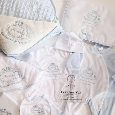 Conjunto de roupa e acessórios para bebé azul e branco com bordados e textura suave.
