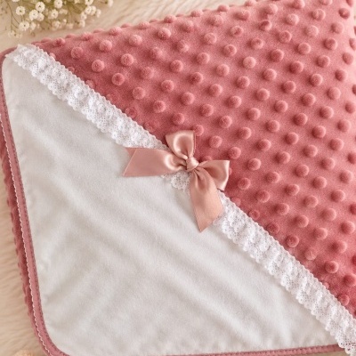 Manta de bebé rosa com textura de bolinhas e laço rosa, urso de peluche com laço e flores brancas