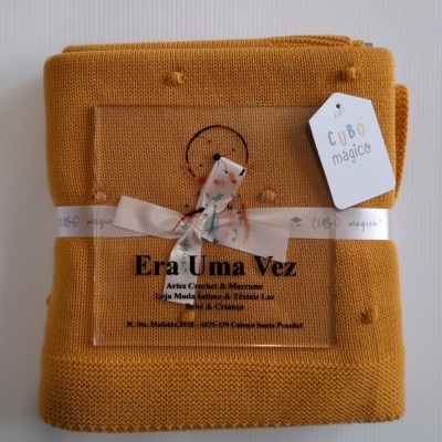 Manta amarela mostarda embrulhada com fita branca e etiqueta 'CUBO mágico'