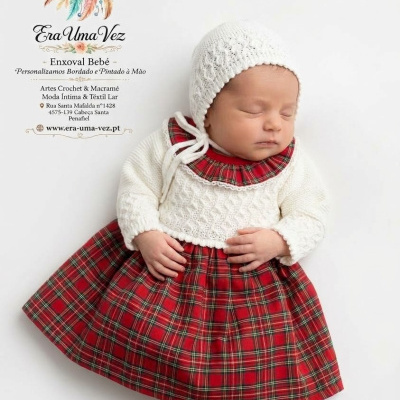 Bebé com vestido xadrez vermelho e camisola branca em fundo branco com texto da marca