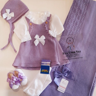 Conjunto de roupa de bebé roxo e branco com gorro, vestido, blusa, meias, sapatinhos e manta.