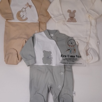 Macacões de bebé em bege, branco e cinza com aplicações bordadas e botões.