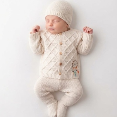 Bebé a dormir com roupa de malha creme e gorro