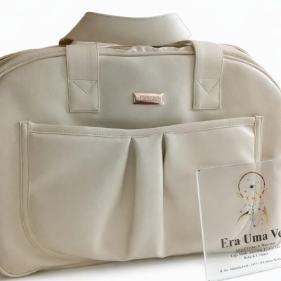 Mala bege com bolso frontal e placa metálica, acompanhada de placa de acrílico com texto e apanhador de sonhos