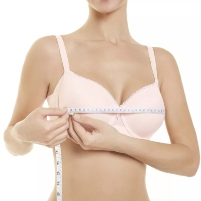 Mulher a medir o peito com fita métrica, veste soutien rosa claro.