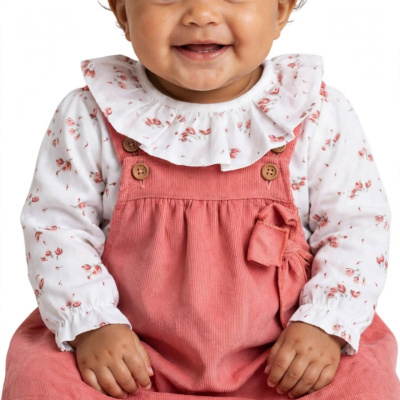 Bebé sorridente vestido com macacão cor de rosa e camisa branca com flores