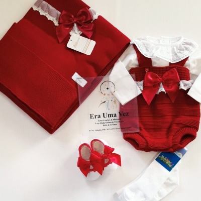 Conjunto roupa bebé com manta, body, bombachos, meias e sapatinhos, em tons vermelhos e brancos com laços e rendas.