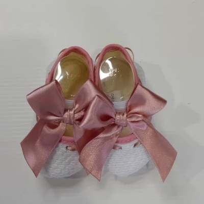 Roupinhas de bebé brancas com laços rosa em tecido, sobre superfície branca.