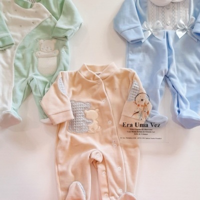 Três macacões de bebé em verde claro, azul claro e rosa claro, com detalhes bordados e laços, sobre fundo branco e cartão de loja Era Uma Vez.