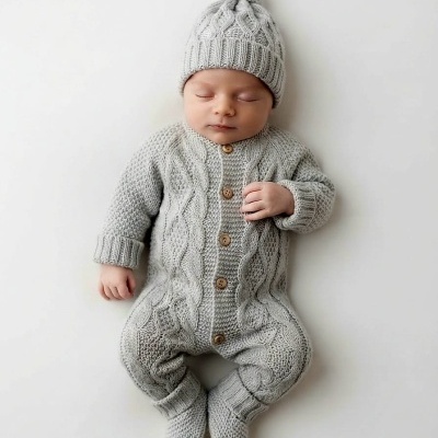Bebé com fato de malha cinzento e gorro com pompom deitado