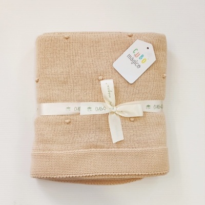 Manta de malha bege dobrada com etiqueta branca ao lado