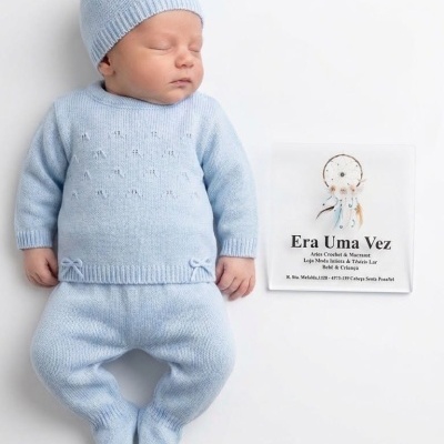 Bebé com roupa de malha azul claro deitado, placa com texto em português ao lado