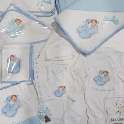 Conjunto de roupa de bebé branco e azul com padrão de sapatinhos azuis e ilustração de bebé.