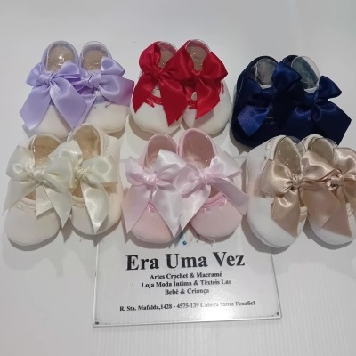 Sete pares de sapatinhos de bebé em tecido com laços coloridos, com placa de acrílico de loja