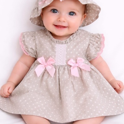 Bebé com vestido bege de bolinhas brancas e chapéu combinando com laço cor-de-rosa
