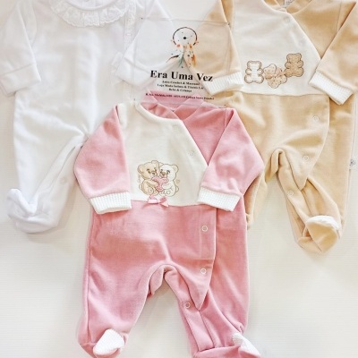 Tres macacões de bebé em branco, bege e rosa com bordados e gola rendada, em fundo branco.